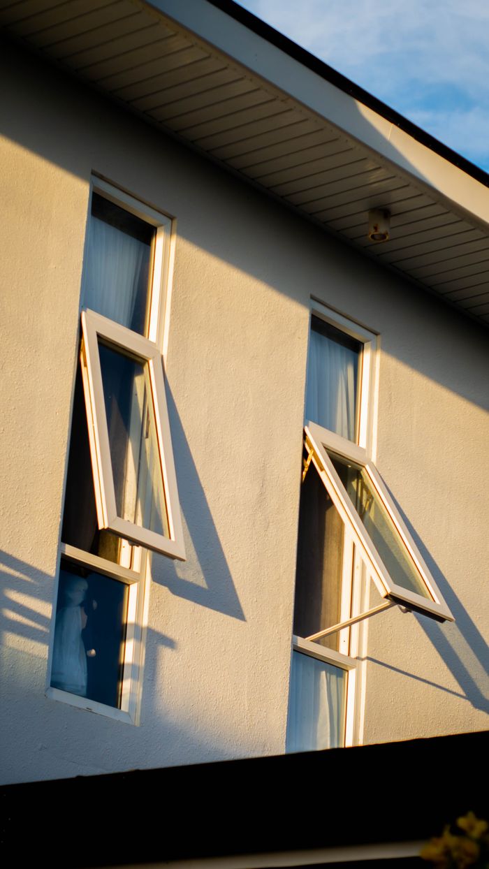Close-up view of a white building with open windows at sunset, highlighting architectural details.