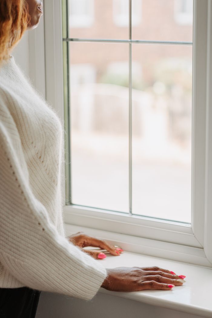 Adult woman in a sweater looking out a window, indoors, during the day.